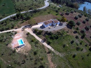 Vista aerea di una proprietà con piscina, una casa con tetto in tegole e una strada tortuosa nelle vicinanze.