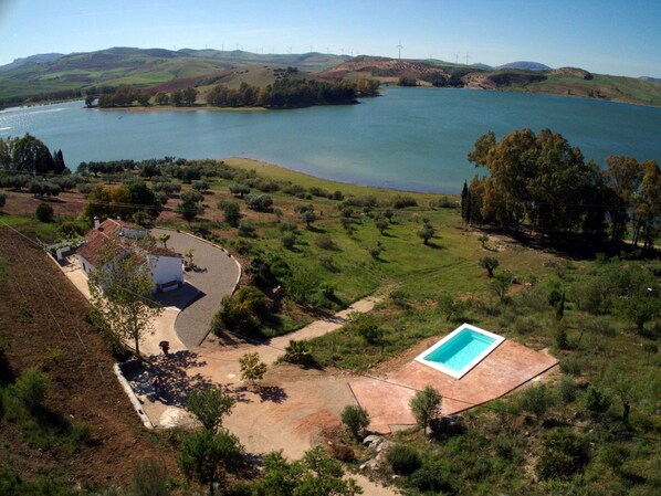 Zona residenziale con piscina, una casa e vista su un lago con turbine eoliche sullo sfondo.