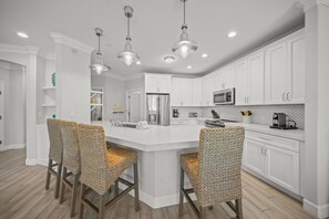 A modern kitchen with white cabinetry, a central island with bar stools, and pendant lighting. - Steps from Beach. Roof Top Deck-Gulf Views. Shared Heated Pool (Siesta Key)