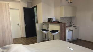 Ett hotellrum med en säng, två vita barstolar, ett litet pentry och en dörr som leder till ett annat rum.