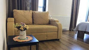 Ett vardagsrum med en beige soffa, ett litet bord med en färgglad, vävd bordsduk och en vas med blommor.