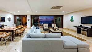 Amplia sala de estar con sofá grande, mesa y sillas de comedor, televisor de pantalla plana y balcón con vistas.