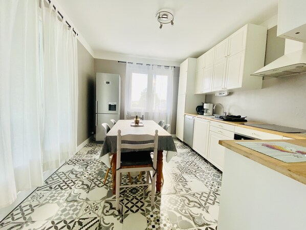 Una cocina compacta con armarios blancos, un refrigerador y una mesa de comedor con sillas.