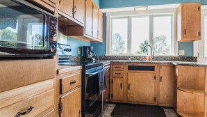 A kitchen with wooden cabinets, a microwave, an oven, and a sink. - Located Directly On Rockland Harbor (Rockland)