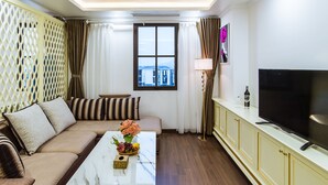 Una sala de estar con un sofá, una mesa de centro con flores, un televisor y una ventana con cortinas.