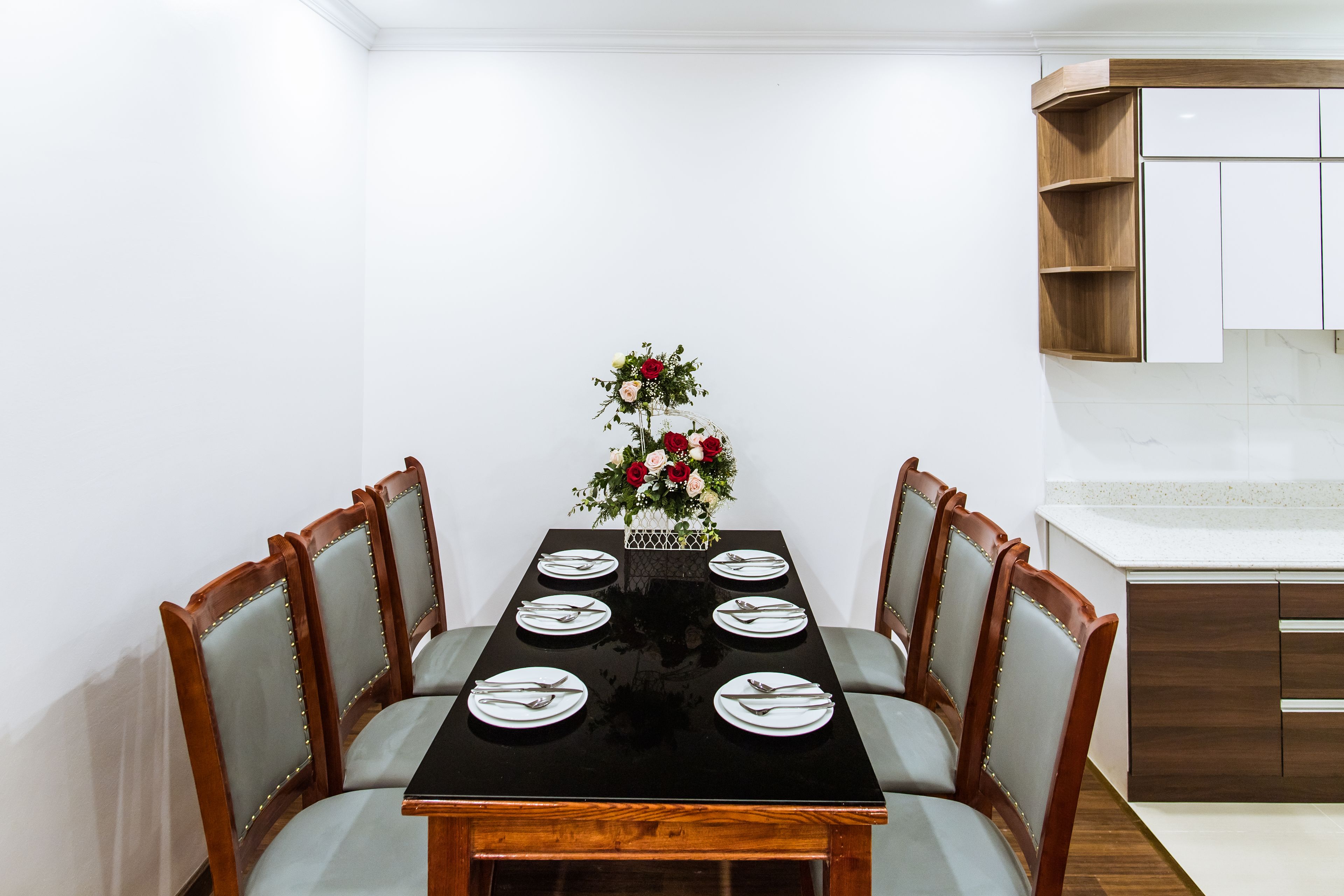 A dining table with six chairs, a vase of flowers, and a kitchen area with wooden cabinets and a countertop.