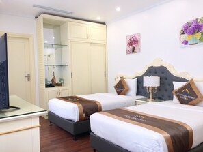 A hotel room with two beds, a desk, a TV, a wardrobe, and a painting on the wall. - Sun Halong Hotel (Ha Long)