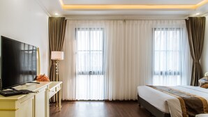 Una habitación de hotel con una cama grande, un escritorio con televisor de pantalla plana y un ventanal con cortinas.