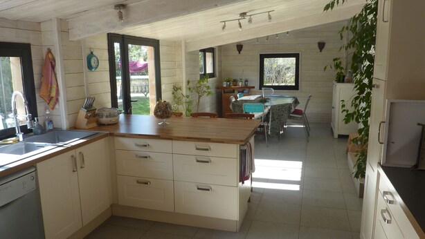A modern kitchen with white cabinetry, a wooden countertop, and a dining area with a table and chairs. - house between vineyards and garrigue (Vénéjan)