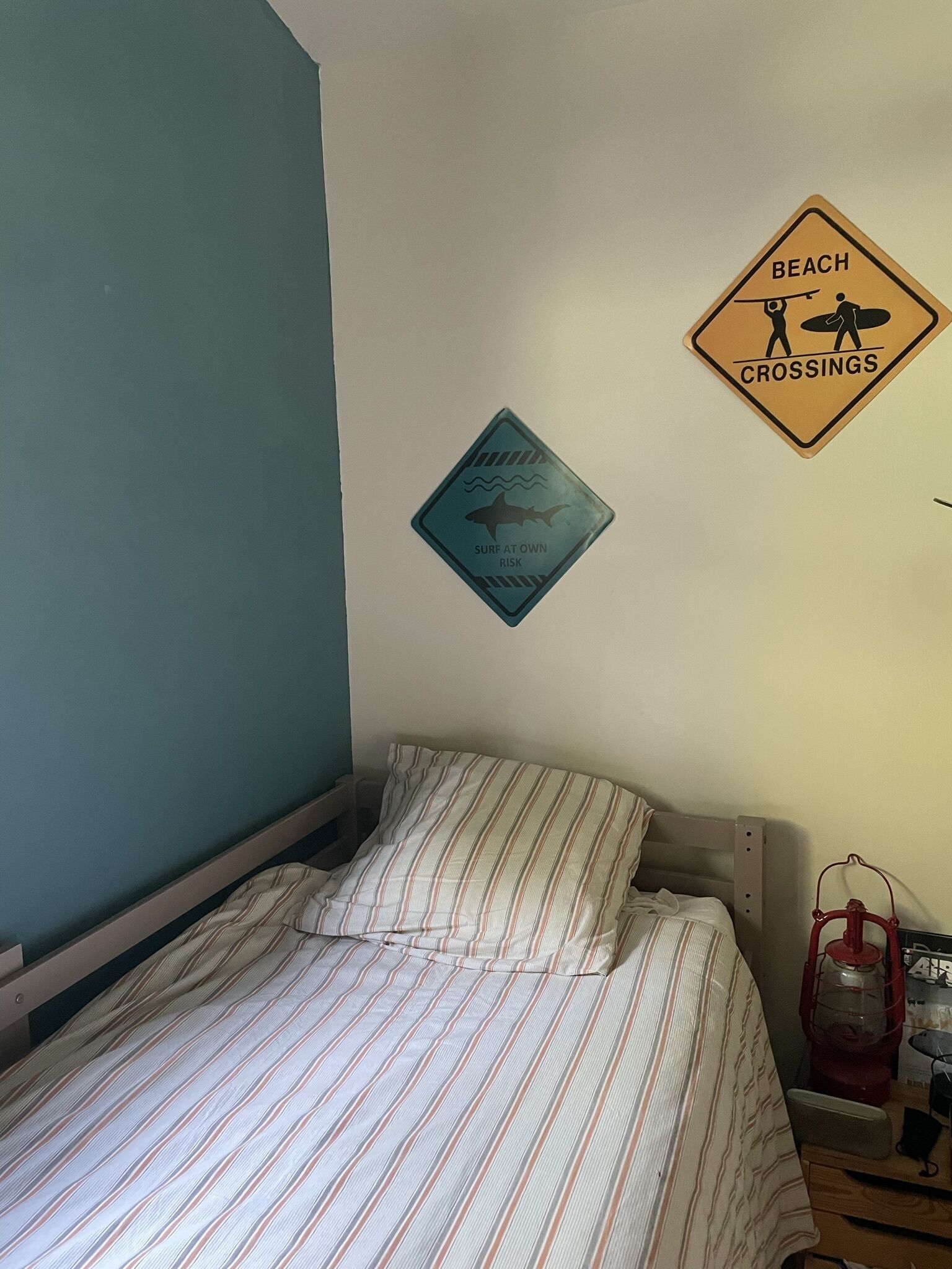 Una camera da letto con un letto, un cartello fissato al muro che indica i passaggi per la spiaggia e un segnale di attenzione: surfare a proprio rischio.