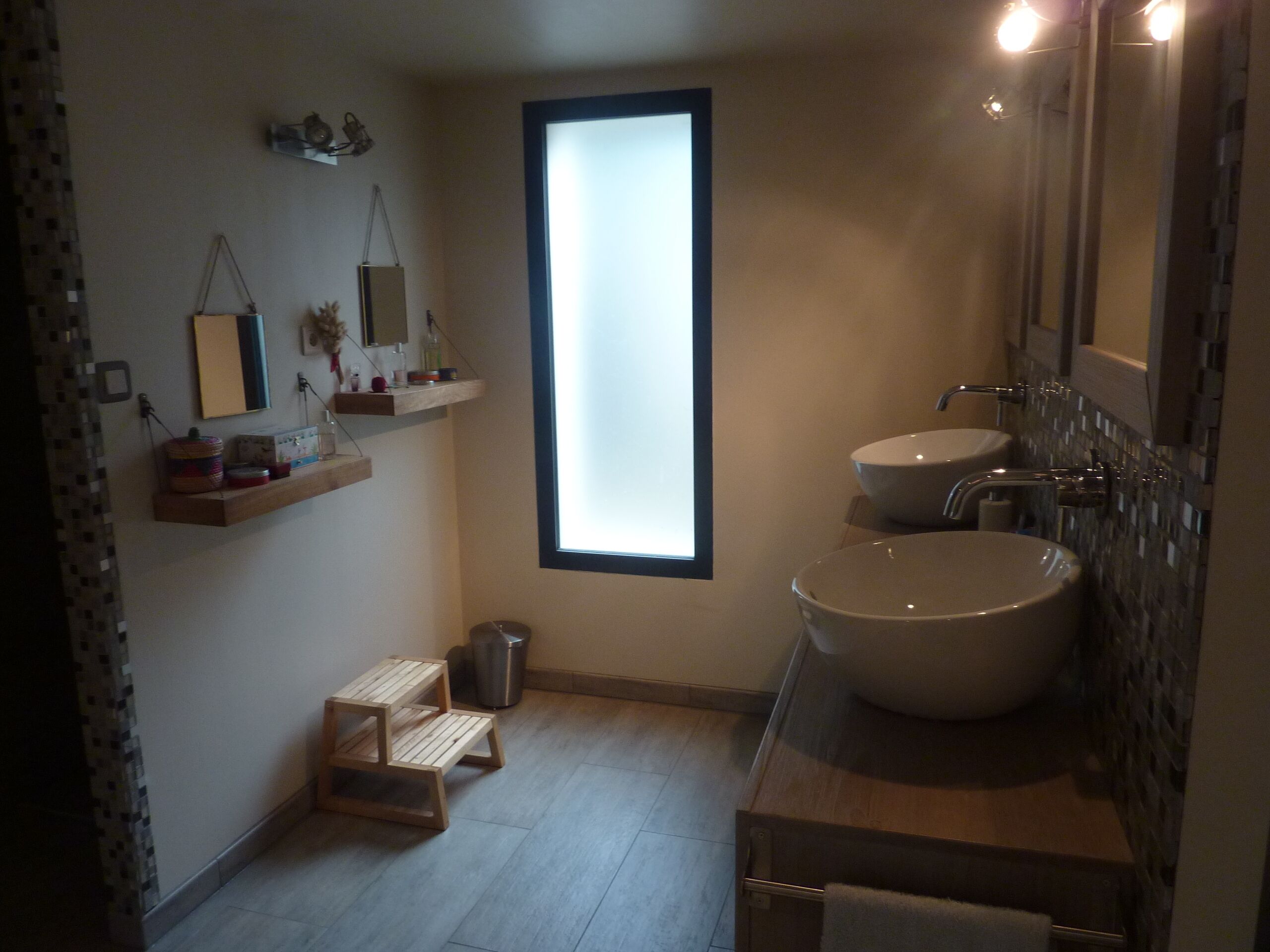 A bathroom with two sinks, a window, a mirror, and wooden shelves with toiletries.
