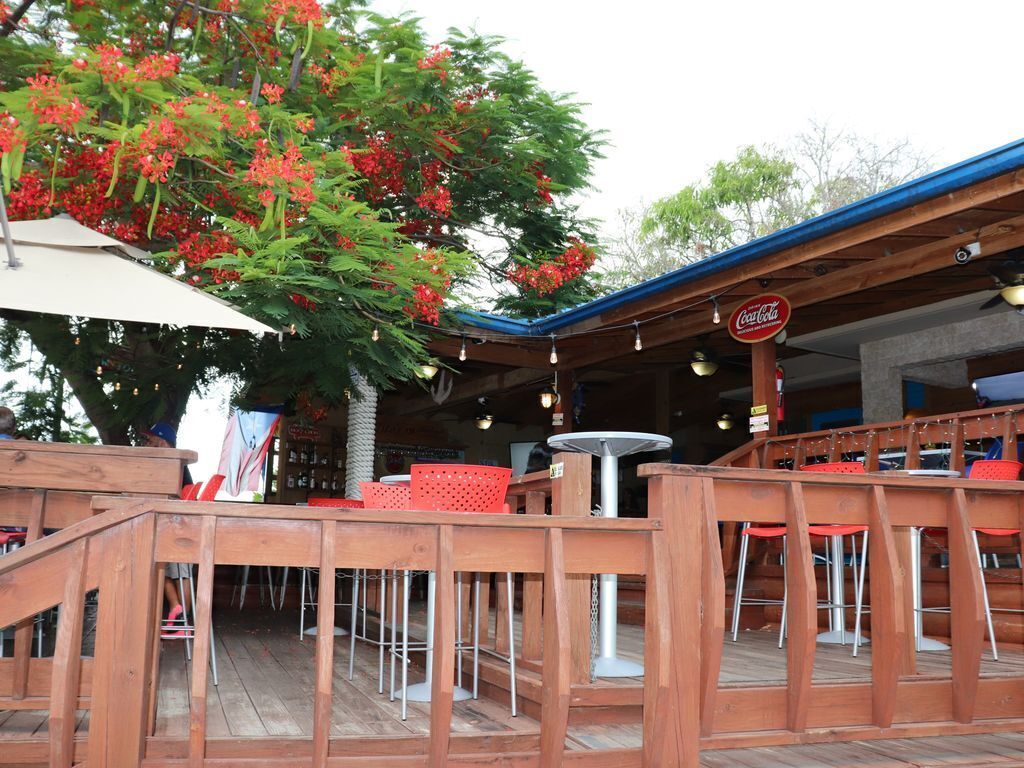 Een terras buiten met houten terras, rode stoelen en tafels.