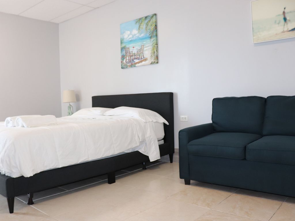 A bedroom with a bed, a dark-colored sofa, and two wall-mounted artworks depicting beach scenes.