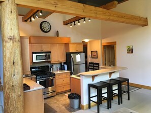 A compact kitchen with wooden cabinets, a microwave, a stove, a refrigerator, and a small island with stools. - Vacation Penthouse Condo in a Ski and Mountain Bike Resort (Red Mountain Village)