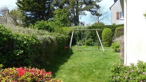 Un giardino curato con altalene, un edificio bianco e vegetazione rigogliosa.