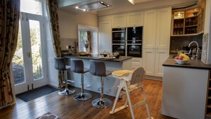 A modern kitchen with white cabinets, a central island with bar stools, and a wooden chair.