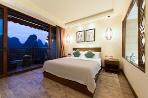 A hotel room with a large bed, a nightstand, a window with a view of mountains, and a balcony with chairs. - Yangshuo Lightheart Homestay (Guilin)
