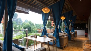A restaurant with wooden furniture, blue curtains, and a view of greenery. - Yangshuo Lightheart Homestay (Guilin)