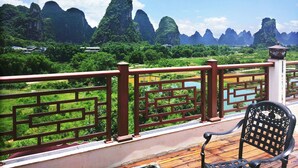 A balcony with a wooden railing overlooking a lush landscape with tall, green mountains and a river. - Yangshuo Lightheart Homestay (Guilin)