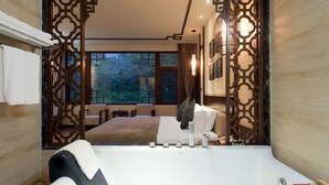 A modern hotel room with a large bed, a sitting area with a view of the outdoors, and a bathtub with toiletries. - Yangshuo Lightheart Homestay (Guilin)