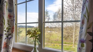 A window with a clear view of a rural landscape, a vase with flowers, and floral curtains. - Peaceful, relaxing  lodge for 2 set in countryside (Elgin)