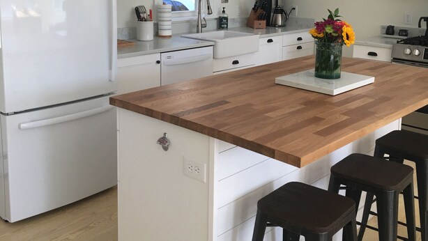 A modern kitchen with white cabinetry, a wooden island, and bar stools. - Pond House - Donnell's Pond in Franklin, Maine (Franklin)