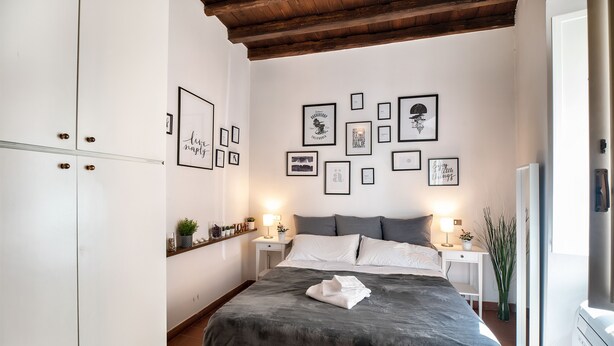 Ein Schlafzimmer mit einem Bett, Nachttischen, einem Schreibtisch und einer Wand mit gerahmten Bildern.