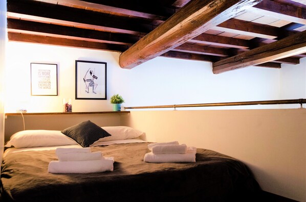 Une chambre avec un plafond en bois, un lit avec des oreillers blancs et noirs, et deux tableaux encadrés accrochés au mur.