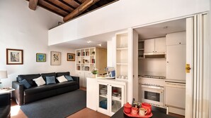 Ein modernes Wohnzimmer mit einem schwarzen Sofa, einem Couchtisch mit roten Tassen und einer Küchenzeile mit weißen Geräten.
