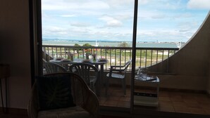 A balcony with a view of a body of water and a bridge, furnished with chairs and a table. - Spacious T3 with large terrace SEA VIEW (Le Grau-du-Roi)