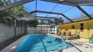Piscina coberta com teto de vidro, cercada por espreguiçadeiras e um edifício amarelo.