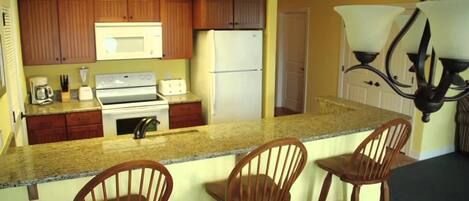 A kitchen with wooden cabinets, a microwave, a refrigerator, a stove, and a bar area with chairs.