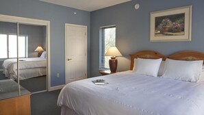 Une chambre à coucher avec un grand lit, une table de chevet avec une lampe, un miroir et une porte.