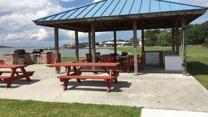 Un espace pique-nique abrité, équipé de bancs et d’un barbecue, avec vue sur une étendue d’eau.