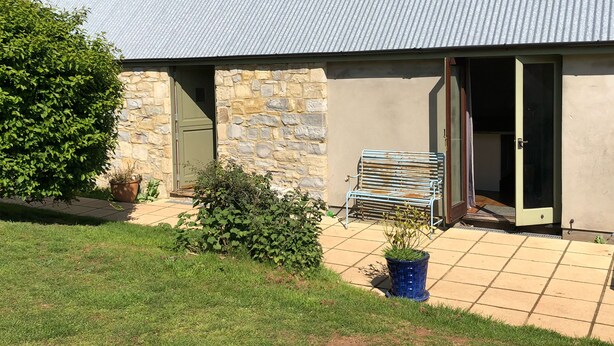 Un bâtiment doté d’une façade en pierre, d’un toit en métal et d’un patio carrelé avec un banc et des plantes en pot.
