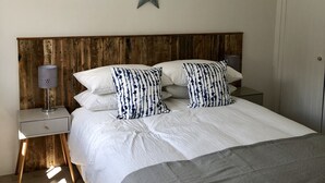 Une chambre avec une tête de lit en bois, une décoration en forme d’étoile sur le mur, une table de chevet avec une lampe et des coussins à rayures.