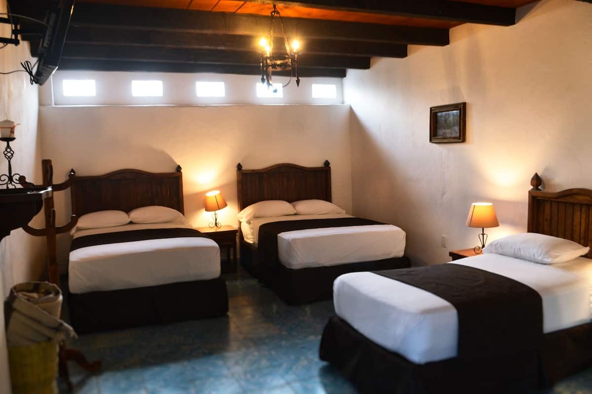 Ein Hotelzimmer mit drei Einzelbetten, Holz-Kopfteilen und Nachttischlampen.