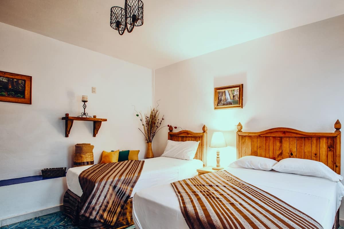 Ein Hotelzimmer mit zwei Betten, einem hölzernen Kopfteil, einem Nachttisch mit Lampe, einer kleinen Ablagefläche mit Kerze und einem gerahmten Bild an der Wand.