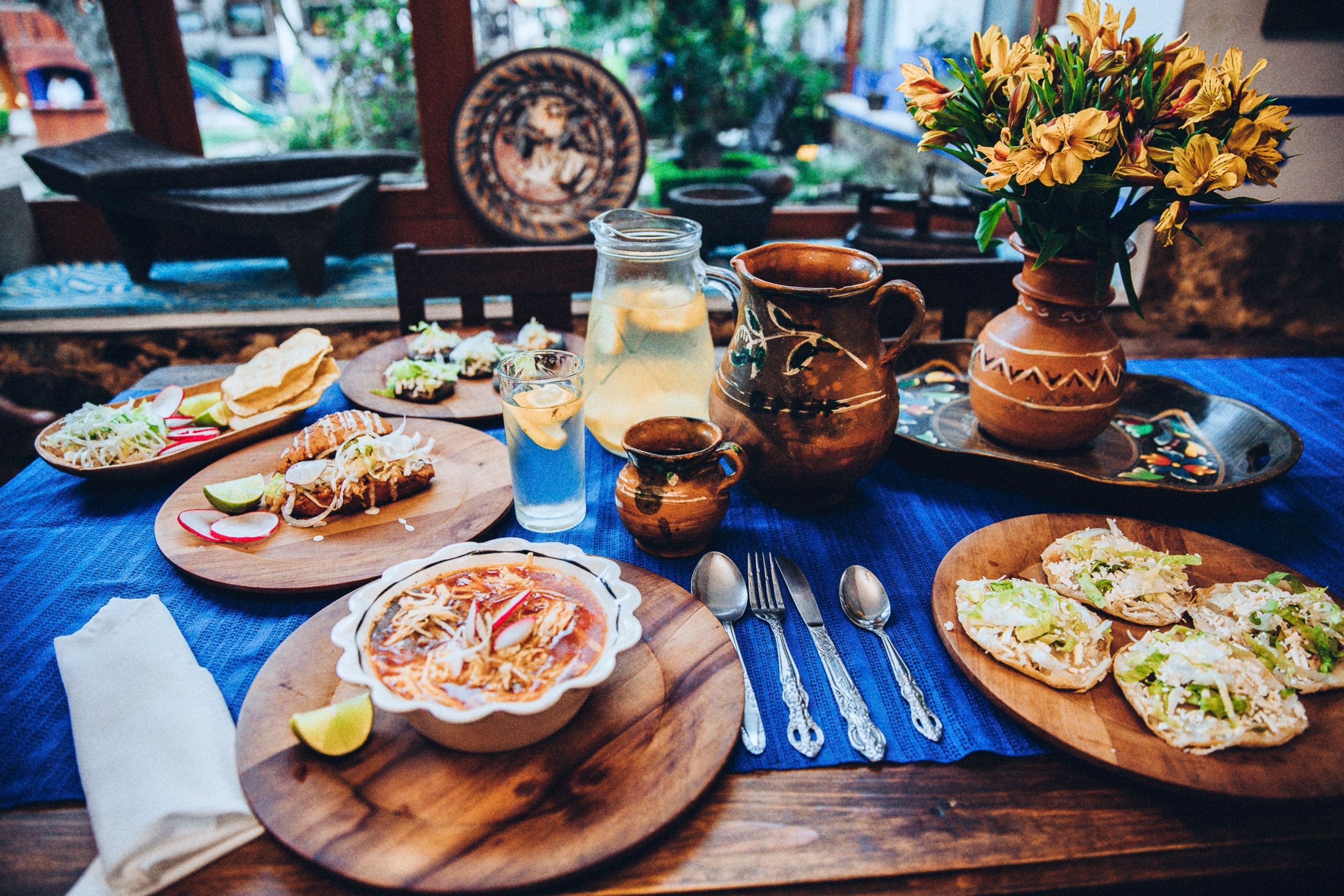 A table set with various dishes, including tacos, a bowl of soup, and a pitcher of lemonade.