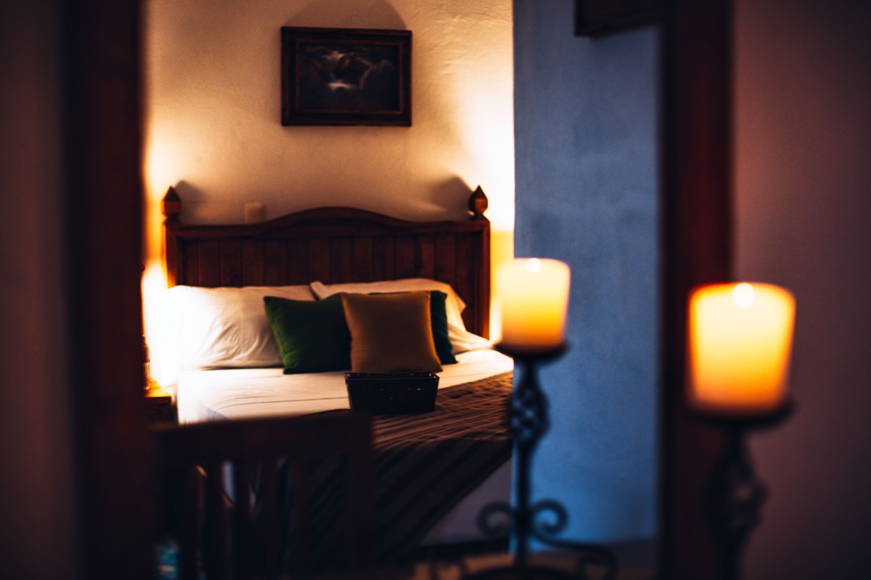 A dimly lit hotel room with a wooden bed, pillows, and two lit candles on a bedside table.