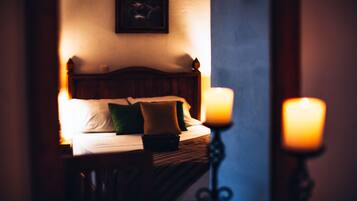 A dimly lit hotel room with a wooden bed, pillows, and two lit candles on a bedside table.