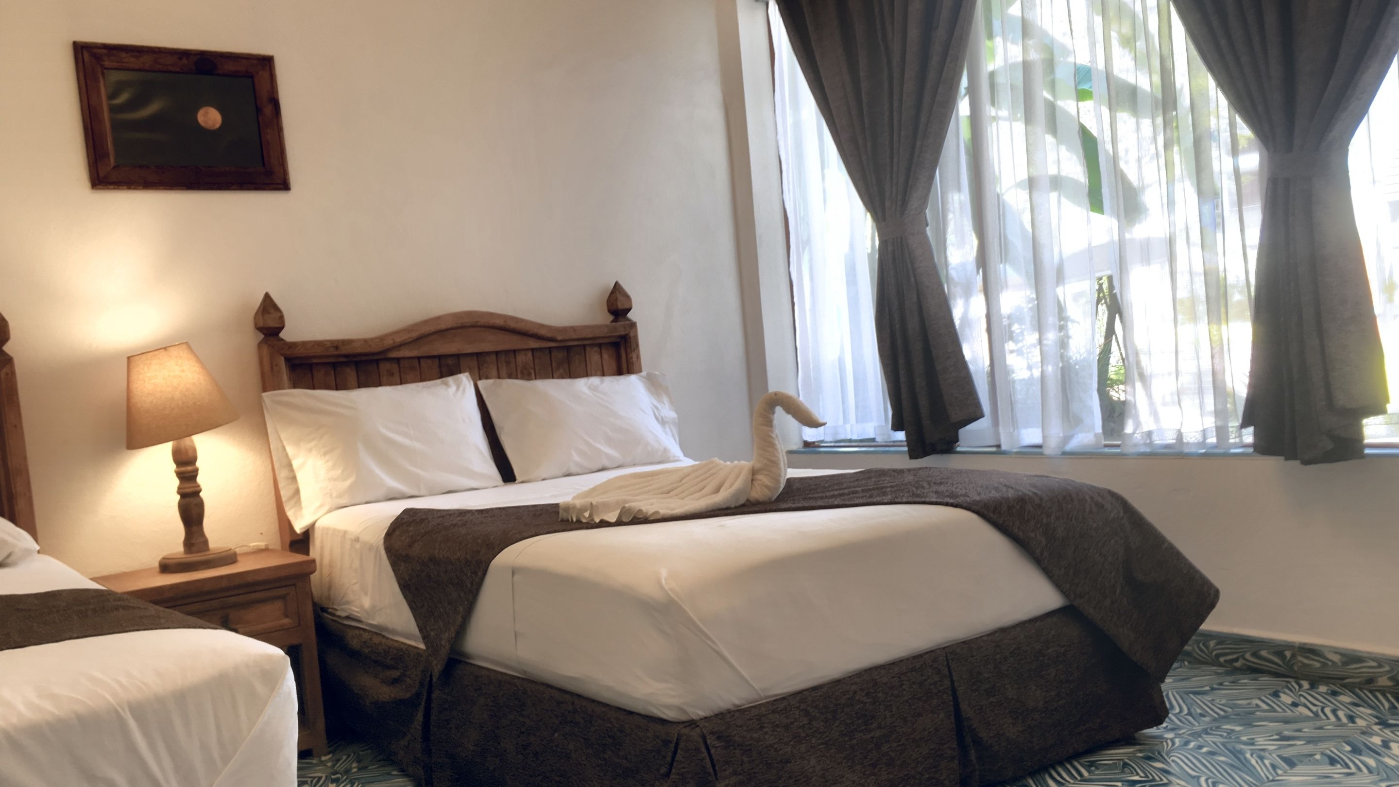 A neatly made bed with a swan-shaped pillow, a wooden headboard, a bedside lamp, and a window with curtains.