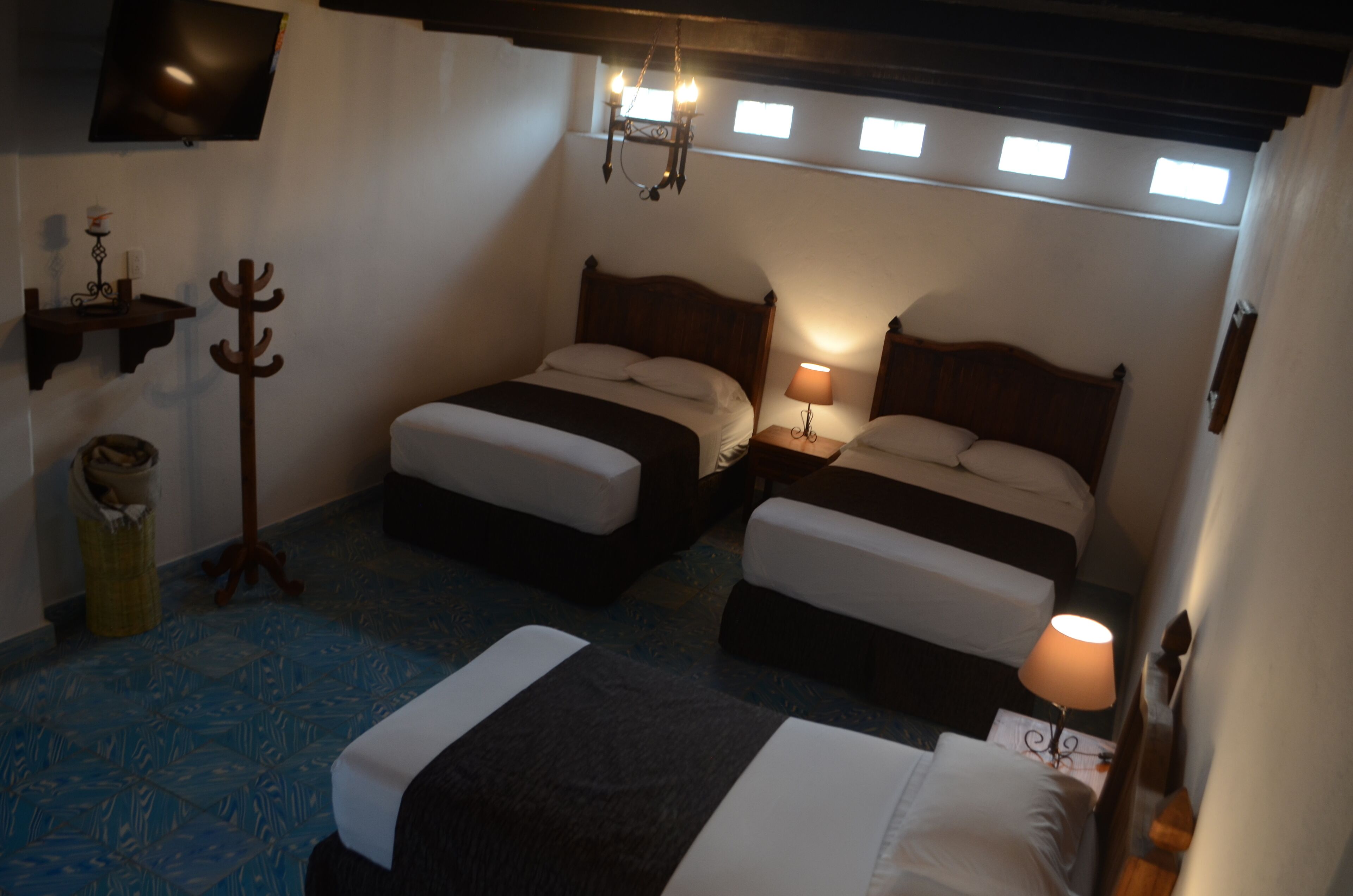 A room with two beds, a wooden coat rack, a lamp, and a television on the wall.