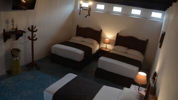 A room with two beds, a wooden coat rack, a lamp, and a television on the wall.