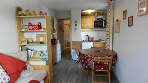 Un espacio habitable compacto con sofá, una mesa de comedor con sillas, una zona de cocina con microondas y un mueble pequeño.