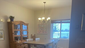 A kitchen with a wooden dining table, chairs, a cabinet with glass doors, a chandelier, and a window with a view of the outdoors. - A Grand  Teton getaway (Driggs)