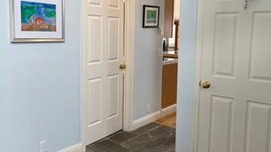 A hallway with two white doors, a framed painting on the left wall, and a blue object hanging on the right door. - A Grand  Teton getaway (Driggs)