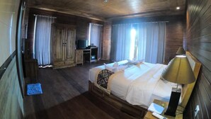 Una habitación de hotel con techo de madera, una cama con ropa blanca, un escritorio con computadora y cortinas en las ventanas.