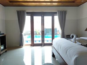 A hotel room with a bed, a TV, and a view of a pool through a glass door.