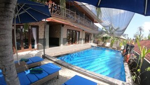 Una piscina con agua azul, rodeada de sillas de descanso y sombrillas.